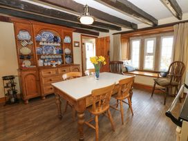 A dining room with a wooden table and chairs a cupboard with blue and white dishes a window seat with cushions and wooden beams on the ceiling at Pagecroft Cottage in Haydon Bridge