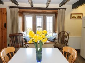 A dining area with a white table and a vase of yellow flowers in front of a window seat with cushions at Pagecroft Cottage in Haydon Bridge
