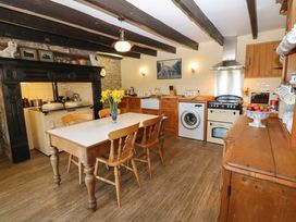A kitchen with wooden cabinets dining table chairs stove and washing machine at Pagecroft Cottage in Haydon Bridge