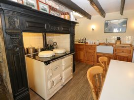 A kitchen with wooden cabinets a white stove with black hood wooden chairs and a white table at Pagecroft Cottage in Haydon Bridge