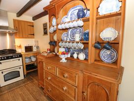 A kitchen with a wooden dresser holding blue and white china and a stove next to a microwave on a wooden stand at Pagecroft Cottage in Haydon Bridge