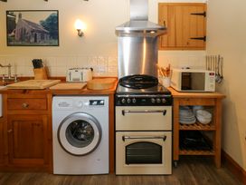 A kitchen with a washing machine stove microwave wooden countertops and shelves at Pagecroft Cottage in Haydon Bridge