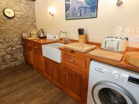 A kitchen with wooden cabinets a white sink a washing machine and various kitchen appliances at Pagecroft Cottage in Haydon Bridge