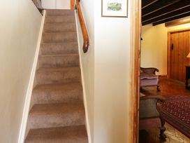 A carpeted staircase with a wooden handrail next to a room with armchairs a rug and wooden door at Pagecroft Cottage in Haydon Bridge
