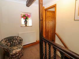 A hallway with a floral armchair a radiator wooden door wooden banister and a vase with pink flowers in a window at Pagecroft Cottage in Haydon Bridge