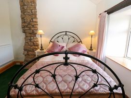 A bedroom with a black metal bed frame pink pillows a stone wall feature and two lamps at Pagecroft Cottage in Haydon Bridge