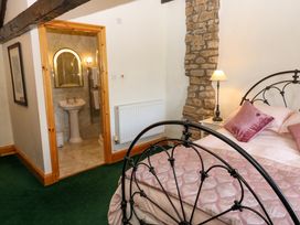 A bedroom with a metal bed frame pink bedding stone wall lamp and an open doorway to a bathroom at Pagecroft Cottage in Haydon Bridge