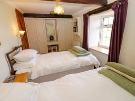 A bedroom with two single beds white bedding green pillows beige wardrobes wooden door and window with purple curtains at Pagecroft Cottage in Haydon Bridge