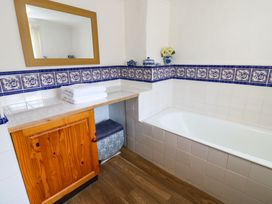 A bathroom with a wooden cabinet white tiles blue decorative tile border and a bathtub at Pagecroft Cottage in Haydon Bridge