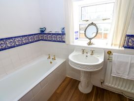 A bathroom with a bathtub a pedestal sink a window with curtains and decorative blue tiles at Pagecroft Cottage in Haydon Bridge