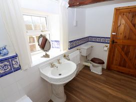 A bathroom with a white pedestal sink and toilet with a brown seat a wooden door and blue decorative tile trim at Pagecroft Cottage in Haydon Bridge
