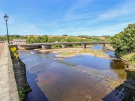A river with a stone bridge and a modern bridge over it with trees and hills in the background at Pagecroft Cottage in Haydon Bridge