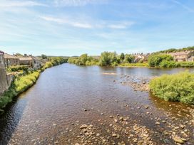 A river with stones in the water and houses along the banks at Pagecroft Cottage in Haydon Bridge