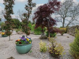 A garden with gravel pathways various trees potted flowers and a stone lantern at Pagecroft Cottage in Haydon Bridge