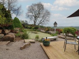 A garden with a pond a stone bench plants a birdhouse and outdoor chairs at Pagecroft Cottage in Haydon Bridge