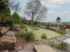A garden pond surrounded by stone pathways shrubs and a birdhouse on a post at Pagecroft Cottage in Haydon Bridge