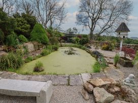A garden with a pond covered in green algae a bench trees plants and a birdhouse at Pagecroft Cottage in Haydon Bridge