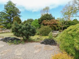 A garden with trees shrubs a stone path and a pond at Pagecroft Cottage in Haydon Bridge