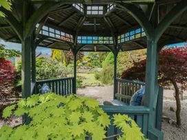 A wooden gazebo with blue cushions surrounded by greenery and a garden view at Pagecroft Cottage in Haydon Bridge