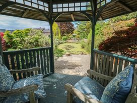A garden view from a wooden gazebo with cushioned chairs overlooking a pond and plants at Pagecroft Cottage in Haydon Bridge