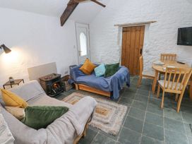 A living room with two sofas a small table with a lamp a wood-burning stove a wooden dining table with chairs a television on the wall and a wooden door at Anchor Light in Castlemartin near Pembroke