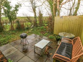 An outdoor patio with a charcoal grill table bench and wooden fence surrounded by trees and greenery at Anchor Light in Castlemartin near Pembroke