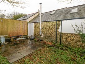 A garden patio with a bench table and barbecue grill next to a stone wall at Anchor Light Castlemartin near Pembroke