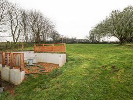 A grassy backyard with a wooden fence patio area and trees at Anchor Light Castlemartin near Pembroke