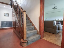 A staircase with carpet going up with a brown wooden railing and a doorway to a room with a sofa and fireplace at Segrwyd Uchaf in Denbigh near Conwy