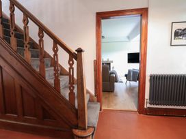 A wooden staircase with grey carpeted steps next to a doorway leading to a living room with wooden flooring at Segrwyd Uchaf in Denbigh near Conwy