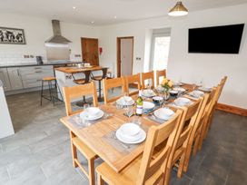 A dining area with a wooden table set for ten with dishes and glasses next to a kitchen with stools at Segrwyd Uchaf in Denbigh near Conwy