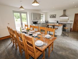 A dining area with a wooden table set with dishes and glasses and a kitchen with grey cabinets and an island at Segrwyd Uchaf in Denbigh near Conwy
