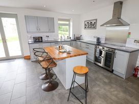 A kitchen with grey cabinets a kitchen island with wooden top and bar stools a stainless steel oven and cooker hood at Segrwyd Uchaf in Denbigh near Conwy