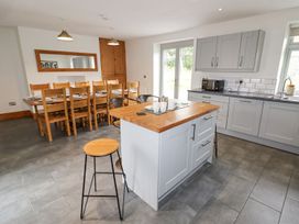 A kitchen with an island and bar stools and a wooden dining table with chairs at Segrwyd Uchaf in Denbigh near Conwy
