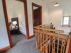 An upstairs hallway with wooden railing a door leading to a bedroom with a bed and bedside table with lamp and a small window at Segrwyd Uchaf in Denbigh near Conwy