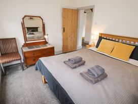 A bedroom with a wooden bed, towels on the bed, a wooden dresser with a mirror, a lamp, and a brown chair at Segrwyd Uchaf in Denbigh, near Conwy