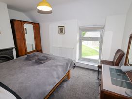 A bedroom with a bed covered with gray blankets a wooden wardrobe with a mirror a window a brown chair and a wooden dresser with a lamp at Segrwyd Uchaf Denbigh near Conwy