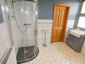 A bathroom with a curved glass shower enclosure a wooden door a window a gray vanity with a white sink and patterned floor tiles at Segrwyd Uchaf in Denbigh near Conwy
