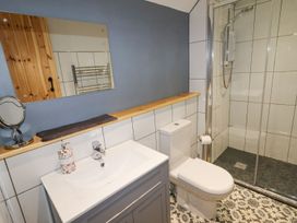 A bathroom with a sink, toilet, shower area with glass door, and mirror at Segrwyd Uchaf in Denbigh near Conwy