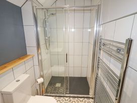 A bathroom with a shower enclosure a toilet a wooden shelf and a chrome towel radiator at Segrwyd Uchaf in Denbigh near Conwy
