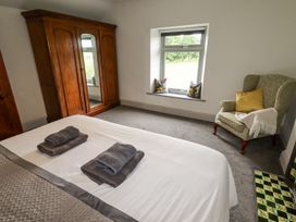 A bedroom with a bed, wooden wardrobe, armchair, and a window with cushions at Segrwyd Uchaf in Denbigh near Conwy