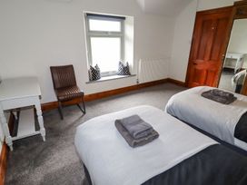 A bedroom with two single beds with folded towels a wooden door a white desk and a brown chair near a window with pillows at Segrwyd Uchaf in Denbigh near Conwy