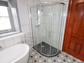 A bathroom with a glass shower enclosure a white bathtub a metal towel rack and a wooden door at Segrwyd Uchaf in Denbigh near Conwy