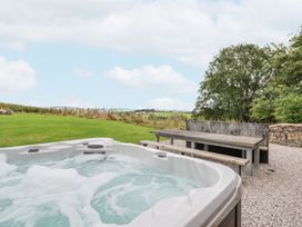 An outdoor hot tub with bubbling water next to a wooden picnic table with benches on gravel with grass and trees in the background at Segrwyd Uchaf in Denbigh near Conwy