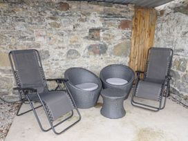 A seating area with two reclining chairs two round chairs with cushions and a small table in a stone wall outdoor space at Segrwyd Uchaf Denbigh near Conwy