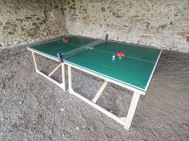 A ping pong table with paddles and a ball in a stone-walled room at Segrwyd Uchaf in Denbigh near Conwy