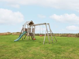 An outdoor wooden playset with a slide and two red swings on a grassy field at Segrwyd Uchaf in Denbigh near Conwy
