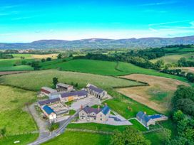 A rural farm property with multiple stone buildings surrounded by green fields and hills at Segrwyd Uchaf in Denbigh near Conwy