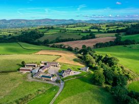 An aerial view of a farmhouse with multiple buildings surrounded by green fields and hills at Segrwyd Uchaf in Denbigh near Conwy