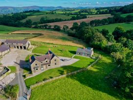 A rural farmhouse with outbuildings and fenced yard surrounded by green fields and rolling hills at Segrwyd Uchaf in Denbigh near Conwy